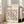 May include: A framed geometric poster with colorful circles split into halves in various bright colors including yellow, pink, blue, purple, orange, and green arranged in a grid pattern. The poster features "BAUHAUS" text at top and sits in a light wood frame leaning against a white wall next to a beige upholstered chair in a bright, naturally-lit room with white walls and wood floors.