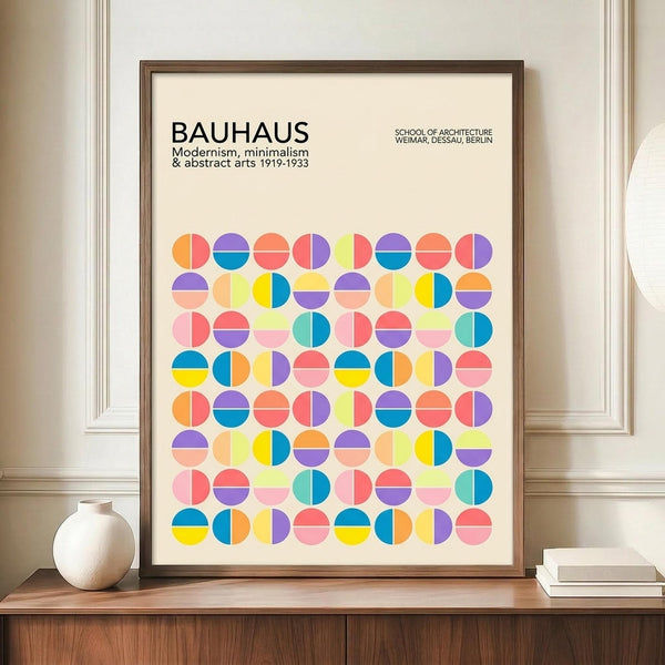 May include: Framed Bauhaus-inspired poster with colorful geometric circles in a grid pattern, featuring vibrant blues, yellows, pinks, and oranges on cream background. Dark wood frame sits on wooden sideboard beside white ceramic vase and stacked books in bright modern interior with white paneled walls.