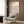 May include: Framed Bauhaus poster with colorful geometric circles in pink, blue, yellow, and orange displayed on wood paneled wall above beige upholstered armchair with patterned throw pillow. Modern brass floor lamp and dark round side table with open book complete the minimalist room setting with light wood floors.