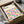 May include: Framed Bauhaus poster with colorful geometric circles in a grid pattern, featuring vibrant blues, yellows, pinks, and purples on cream background. Black frame nestled in cardboard packaging with white tissue paper, sitting on white fabric surface next to partial view of glass bowl.