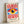 May include: A framed poster print featuring a stylized eye design in Bauhaus style, displayed in a light wooden frame against a white wall. The artwork shows a central eye with yellow iris, dark blue pupil, and white highlight, surrounded by red and white radiating sunburst rays extending from top and bottom. Blue geometric shapes frame the eye horizontally. Text at bottom reads "BAUHAUS 1919-1933 SCHOOL OF ARTS & CRAFTS" in black letters on cream background.