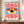 May include: Framed Bauhaus-inspired poster featuring a stylized eye with yellow iris, dark blue pupil, and white highlight, surrounded by radiating red sunburst rays on cream background with blue accents. Displayed on wooden sideboard next to small white ceramic vase and stacked books in modern interior with white paneled walls.