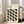 May include: A framed Bauhaus-style poster leaning against a white wall next to a beige upholstered chair. The cream-colored print features geometric leaf-like shapes in black, olive green, and sage arranged in a repeating pattern. Text at top reads "BAUHAUS" and "School of Architecture Weimar, Dessau, Berlin" with "Modernism, minimalism & abstract arts 1919-1933." Light wooden frame, hardwood floors, bright natural lighting from nearby windows.