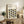 May include: Framed Bauhaus poster with geometric leaf pattern in olive green and dark teal on cream background, displayed on rustic wooden sideboard alongside fern plant, ceramic vases, and leather armchair in neutral-toned living room setting