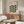 May include: Framed Bauhaus poster with geometric leaf pattern in olive green and black on cream background, displayed above wooden sideboard in modern living room with white sculptural chair, glass coffee table, and minimalist decor