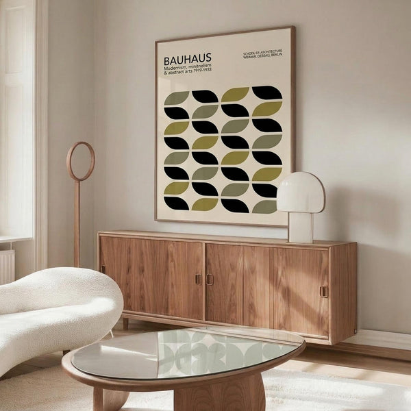 May include: Framed Bauhaus poster with geometric leaf pattern in olive green and black on cream background, displayed above wooden sideboard in modern living room with white sculptural chair, glass coffee table, and minimalist decor
