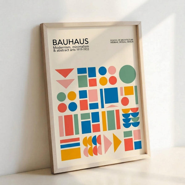 Framed poster featuring colorful geometric shapes in Bauhaus style, with text reading "BAUHAUS Modernism, minimalism & abstract arts 1919-1933" and "SCHOOL OF ARCHITECTURE WEIMAR, DESSAU, BERLIN" at top. Design includes red triangles, blue squares, green and orange circles, and various rectangular forms in bright primary colors arranged in a grid-like composition. Light wood frame leaning against white wall with soft shadows.