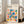 May include: Framed Bauhaus poster with colorful geometric shapes including triangles, circles, squares and rectangles in red, blue, green, orange and pink on cream background. Light wood frame leans against white wall next to beige upholstered chair in bright room with tall windows and hardwood floors.