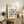 May include: Framed Bauhaus poster with colorful geometric shapes in red, blue, green, orange, and pink displayed on rustic wooden sideboard alongside fern plant, ceramic vase, and books in neutral-toned living room setting with beige upholstered furniture