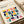 May include: Framed Bauhaus poster print with colorful geometric leaf-like shapes in pink, yellow, orange, navy, teal, and purple arranged in a grid pattern. The cream-colored print features "BAUHAUS" text and "Modernism, minimalism & abstract arts 1919-1933" with "School of Architecture, Weimar, Dessau, Berlin" subtitle. Frame sits on white bedding next to a beige pillow, showing the minimalist mid-century modern design aesthetic.