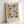May include: Framed geometric art print leaning against white wall featuring colorful semicircles and circles in muted tones of coral pink, sage green, mustard yellow, navy blue, and dusty blue arranged in a grid pattern on cream background, displayed in light wood frame on white surface