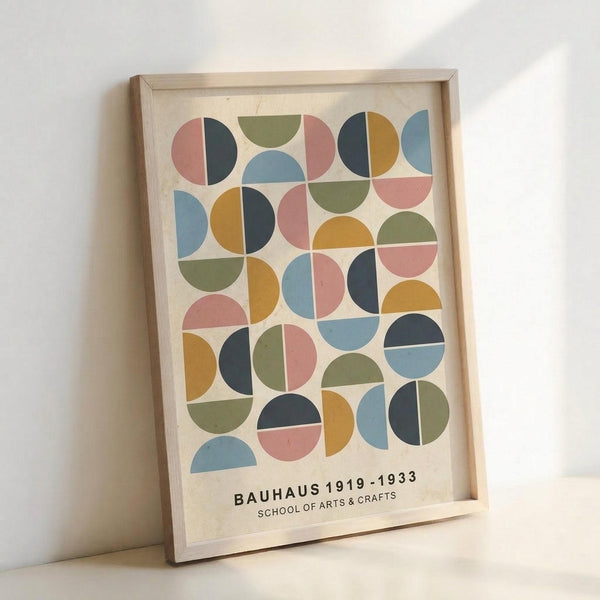 May include: Framed geometric art print leaning against white wall featuring colorful semicircles and circles in muted tones of coral pink, sage green, mustard yellow, navy blue, and dusty blue arranged in a grid pattern on cream background, displayed in light wood frame on white surface