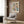 May include: Modern living room mockup showing beige armchair with geometric pillow, gold floor lamp, dark side table with open book, and wood-paneled wall. Framed poster features colorful semicircles in pink, blue, green, yellow, and navy arranged in geometric grid pattern with Bauhaus text below on cream background.