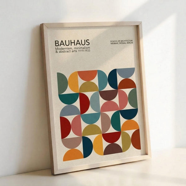 May include: Framed geometric art print in light wood frame leaning against white wall. Design features colorful overlapping semicircles and quarter-circles in earth tones including orange, teal, sage green, burgundy, and mustard yellow on cream background. Text reads "BAUHAUS Modernism, minimalism & abstract arts 1919-1933" and "SCHOOL OF ARCHITECTURE WEIMAR, DESSAU, BERLIN" at top. Modern minimalist home decor styling.