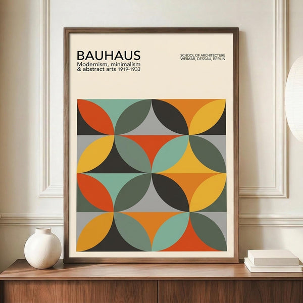May include: Framed Bauhaus-style geometric poster with overlapping circles in orange, yellow, teal, olive green, and black creating repeating patterns. Modern art print displayed on wooden sideboard next to white ceramic vase and stacked books in minimalist room with white walls and crown molding.