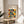 May include: Framed Bauhaus poster with geometric pattern of overlapping circles in orange, yellow, mint green, and gray on cream background, displayed on round wooden side table next to beige upholstered chair with plant shadow cast on white wall behind