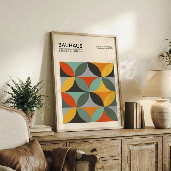 May include: Framed geometric poster with colorful overlapping circles in orange, yellow, teal, and gray displayed on rustic wooden sideboard alongside fern plant, books, and ceramic vase in bright modern living room setting