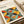 May include: Framed Bauhaus-style poster with overlapping circles in yellow, orange, teal, dark green, and gray creating geometric pattern, displayed on neutral surface with white picture frames and beige decor in soft natural lighting