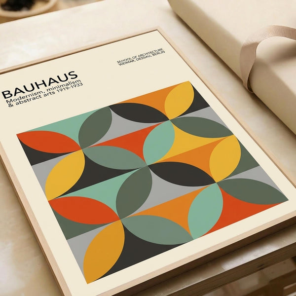 May include: Framed Bauhaus-style poster with overlapping circles in yellow, orange, teal, dark green, and gray creating geometric pattern, displayed on neutral surface with white picture frames and beige decor in soft natural lighting