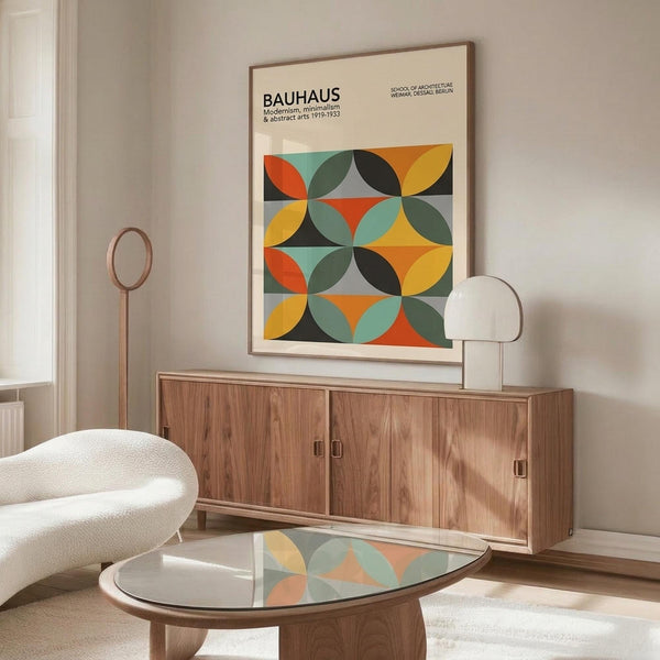 May include: Framed Bauhaus poster with colorful geometric circles in orange, yellow, teal, and black displayed above a mid-century modern wood credenza. Scene shows minimalist living room with white curved chair, glass-top coffee table, and contemporary lamp. The poster features overlapping circular patterns in a grid layout with vintage modernist typography.