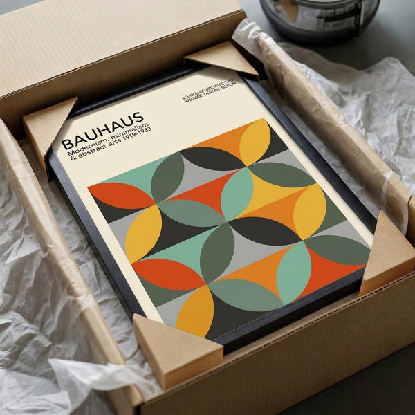 May include: Framed Bauhaus poster with geometric pattern of overlapping circles in yellow, orange, green, and teal colors being unpacked from cardboard shipping box with protective wrapping paper and wooden frame corners visible