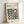 May include: Framed Bauhaus-inspired poster with geometric design featuring dark green circles and pink squares arranged in an abstract pattern. The cream-colored print displays "BAUHAUS" text at top with "Modernism, minimalism & abstract arts 1919-1933" and "School of Architecture Weimar, Dessau, Berlin" below. Natural wood frame leans against white wall on light surface, showing clean minimalist styling typical of Bauhaus movement.