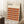 May include: Framed Bauhaus-style poster with geometric pattern of overlapping circles in warm autumn colors - orange, burgundy, brown, and tan - leaning against white wall. Cream-colored frame, positioned next to wooden side table with white coffee cup and saucer, cozy beige throw blanket visible. Clean minimalist room setting with natural lighting creating soft shadows on textured area rug.