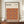 May include: Framed Bauhaus poster with geometric pattern of overlapping circles in warm autumn colors - orange, burgundy, brown, and tan - displayed on wooden sideboard next to white ceramic vase and stacked books in neutral-toned room with white wainscoting