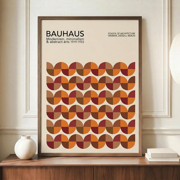 May include: Framed Bauhaus poster with geometric pattern of overlapping circles in warm autumn colors - orange, burgundy, brown, and tan - displayed on wooden sideboard next to white ceramic vase and stacked books in neutral-toned room with white wainscoting