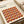 May include: Bauhaus-style poster print displayed on cream-colored surface next to rolled paper tube. The minimalist design features repeating circular patterns in warm autumn colors - burgundy, orange, brown, and tan geometric segments forming overlapping circles. Clean typography at top references modernism and abstract arts from 1919-1933. Smooth matte finish with contemporary aesthetic.