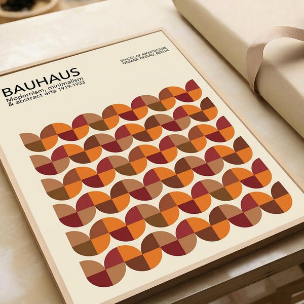 May include: Bauhaus-style poster print displayed on cream-colored surface next to rolled paper tube. The minimalist design features repeating circular patterns in warm autumn colors - burgundy, orange, brown, and tan geometric segments forming overlapping circles. Clean typography at top references modernism and abstract arts from 1919-1933. Smooth matte finish with contemporary aesthetic.