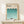 May include: Framed Bauhaus poster with geometric pattern of teal and turquoise semicircles arranged in gradient rows, displayed on light wood surface next to small wrapped gift with twine and greenery. Clean minimalist room setting with cream walls and natural lighting.