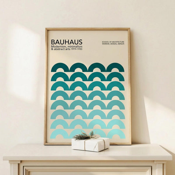 May include: Framed Bauhaus poster with geometric pattern of teal and turquoise semicircles arranged in gradient rows, displayed on light wood surface next to small wrapped gift with twine and greenery. Clean minimalist room setting with cream walls and natural lighting.