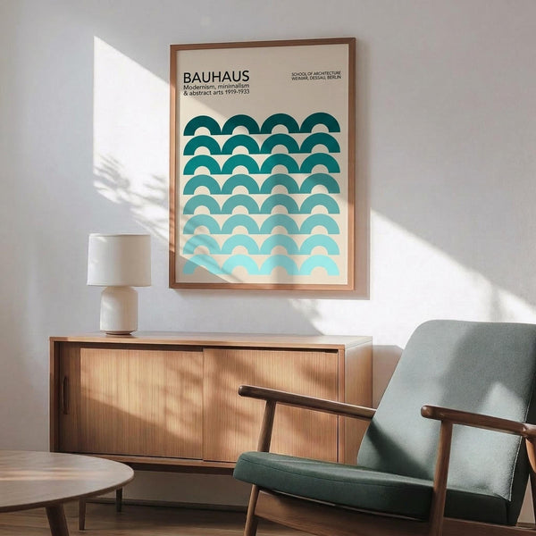 May include: Framed Bauhaus poster with teal gradient wave pattern displayed above mid-century modern wooden credenza. Sage green upholstered armchair with wooden frame sits nearby, along with white ceramic table lamp. Warm natural lighting creates diagonal shadows on white wall, showcasing minimalist interior design with vintage furniture pieces.