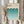 May include: Person holding framed Bauhaus poster with geometric pattern of overlapping semicircles in teal gradient from dark to light blue on cream background. Light wood frame, neutral room setting with dried pampas grass, soft natural lighting through window curtains.