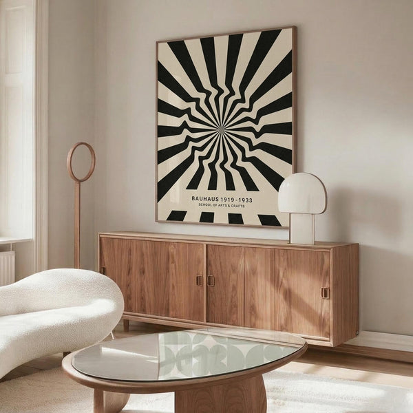 May include: Black and white optical illusion poster with radiating wavy stripes creating a hypnotic sunburst pattern, displayed above a mid-century modern walnut credenza in a minimalist living room. The framed artwork features text at bottom, flanked by a white sculptural chair and brass floor lamp, with a glass-top oval coffee table in foreground.
