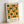 May include: Framed geometric poster with orange and green circular and semi-circular shapes arranged in a grid pattern on cream background, displayed in light wooden frame leaning against white wall. The design features bold mid-century modern style with "BAUHAUS 1919-1933 SCHOOL OF ARTS & CRAFTS" text at bottom.
