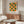 May include: Mid-century modern living room featuring a framed geometric poster with orange and green semicircles arranged in a grid pattern. The artwork hangs above a walnut wood credenza with sliding doors, next to a white curved lounge chair and glass-top oval coffee table. Minimalist decor with neutral walls and natural lighting.