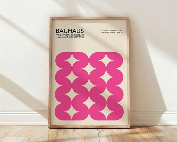 May include: Framed poster with cream background featuring bold pink wavy geometric pattern creating diamond-shaped negative spaces, displayed in light wood frame leaning against white wall on wooden floor with natural window light casting shadows across the scene.