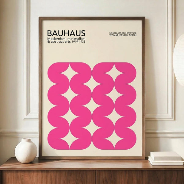 May include: Framed pink and cream Bauhaus-inspired poster with geometric wavy pattern displayed on wooden sideboard next to white ceramic vase and stacked books in elegant room with white paneled walls and warm lighting.