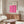 May include: Pink geometric poster with wavy interlocking pattern displayed above wooden sideboard in minimalist living room. Cream textured chair and glass coffee table visible. Poster features "BAUHAUS" text and abstract flowing shapes creating rhythmic design against neutral wall.