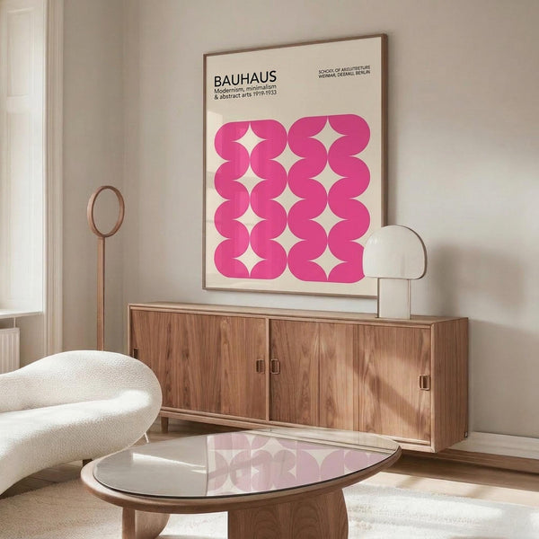 May include: Pink geometric poster with wavy interlocking pattern displayed above wooden sideboard in minimalist living room. Cream textured chair and glass coffee table visible. Poster features "BAUHAUS" text and abstract flowing shapes creating rhythmic design against neutral wall.