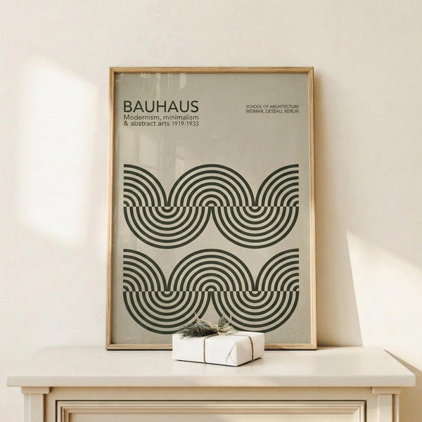 May include: Framed Bauhaus-style poster with geometric black concentric circles pattern on beige background, displayed on light wood console table with small white wrapped gift. Thin natural wood frame, minimalist modern interior setting with white walls and soft natural lighting.