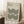 May include: Framed Bauhaus poster with geometric black concentric circles and arcs on cream background, leaning against white wall corner next to wooden block with coffee cup and saucer, beige textured rug visible below