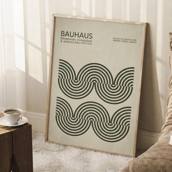 May include: Framed Bauhaus poster with geometric black concentric circles and arcs on cream background, leaning against white wall corner next to wooden block with coffee cup and saucer, beige textured rug visible below