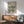 May include: Framed Bauhaus poster with geometric black concentric circles in wave pattern on beige background, displayed above wood sideboard with ceramic lamp. Mid-century modern furniture including teal upholstered armchair with wooden frame, round coffee table. Bright natural sunlight creates dramatic shadows across white wall in minimalist interior setting.