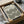 May include: Framed Bauhaus poster with geometric black spiral pattern on cream background, shown in black frame being unpacked from cardboard box with protective wrapping paper on white surface
