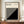 May include: Framed Bauhaus modernist poster with black and white geometric diagonal stripe design displayed on wooden sideboard next to white ceramic vase and books. Features cream background with bold black angular pattern and typography referencing the German design school's history from 1919-1933 across Weimar, Dessau, and Berlin locations.