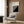May include: Beige armchair with geometric patterned pillow, brass floor lamp, dark wood paneled wall, and framed Bauhaus poster featuring black and white diagonal stripes in modern interior setting with natural lighting from window