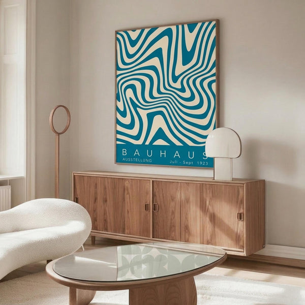 May include: Vintage-style Bauhaus exhibition poster with flowing teal and cream swirled pattern displayed above a mid-century modern wooden credenza in a minimalist living room. White sculptural chair and glass coffee table complete the scene with natural lighting and neutral walls.